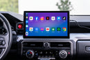 A car's infotainment system with a large touchscreen display showing various app icons, mounted in the dashboard above the climate controls.
